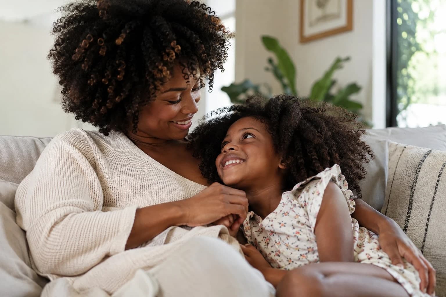 Mãe e filha abraçadas no sofá da sala, sorrindo uma para a outra.